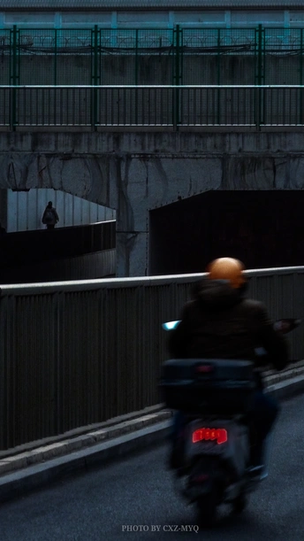 一个人在夜晚骑摩托车在人行桥附近的道路上 有一个男人在驾驶摩托车。