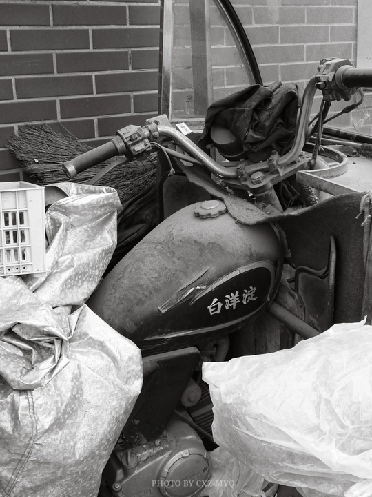 一张黑白照片 展示了一辆停在建筑物旁边 旁边有一个垃圾篮子的旧摩托车。