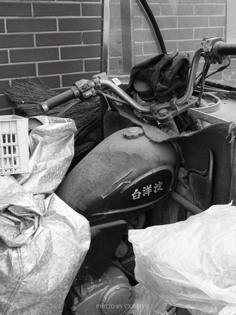 一张黑白照片 展示了一辆停在建筑物旁边 旁边有一个垃圾篮子的旧摩托车。