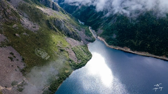 一架飞机在群山和云层环绕的湖面上飞行