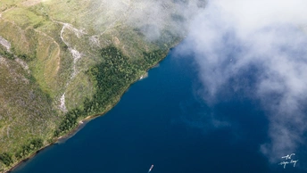 一架飞机在一片水域上空飞行 背景是山脉 天空是云朵