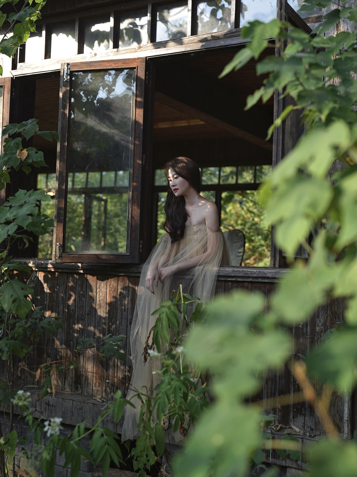 一个穿着长裙的女孩站在树林里的一所房子外面 望着窗外
