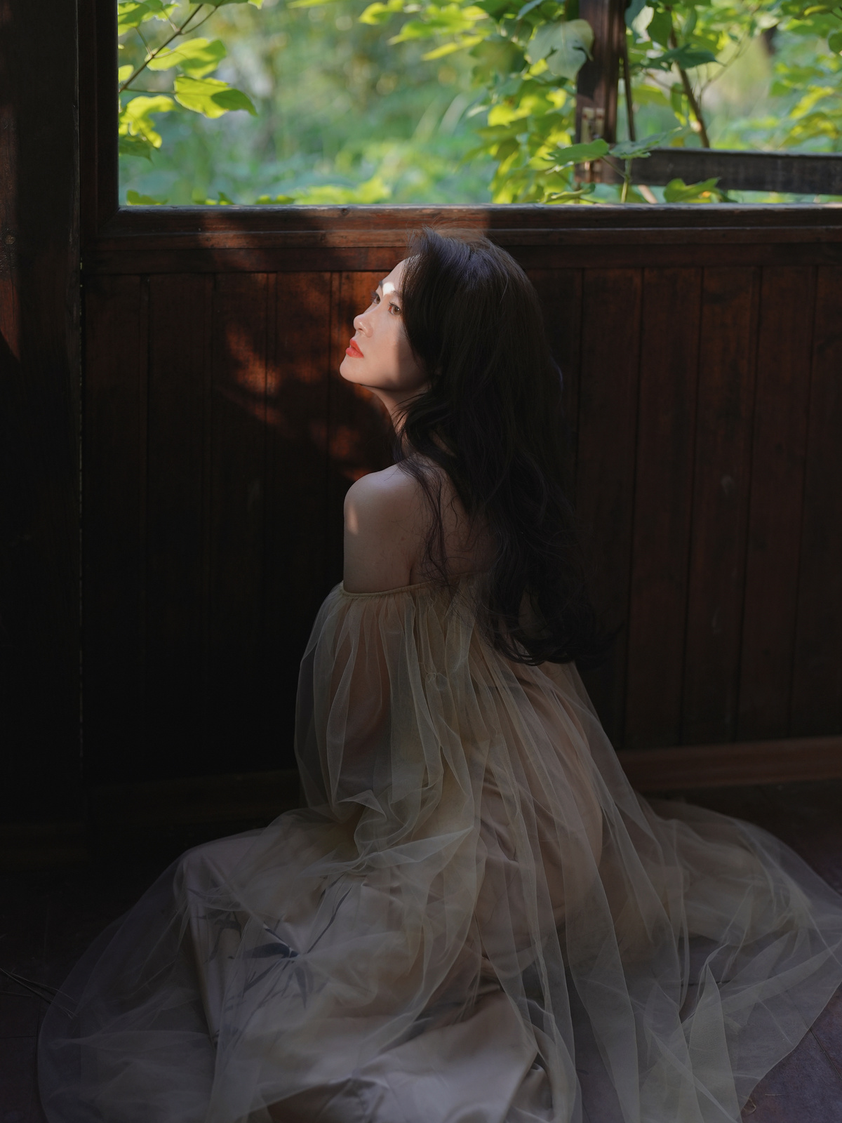 一个穿着连衣裙的年轻女孩坐在窗户边看着外面的光线
