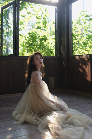 一个穿着白色连衣裙的年轻女子坐在一个有木地板和窗户的阳光充足的房间里