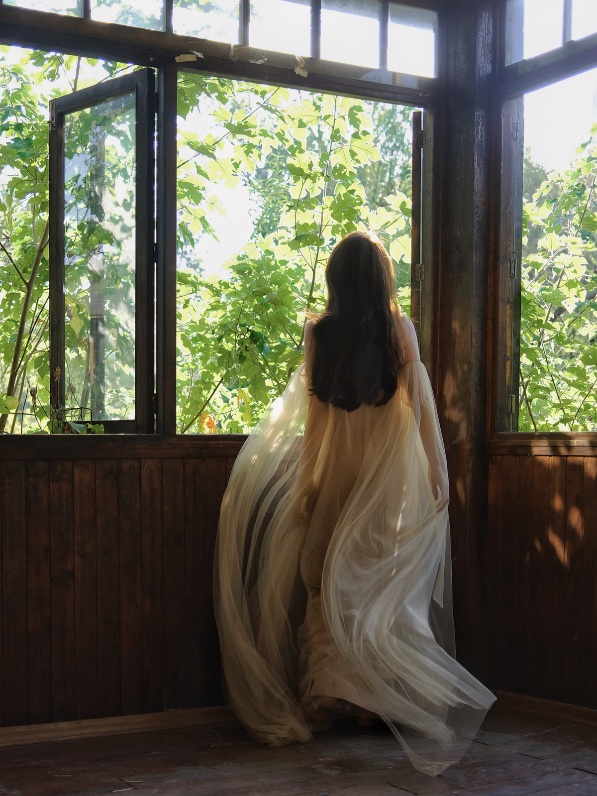 一个穿着白色长裙的女人站在房间里看着窗外