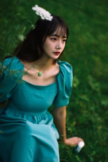 一个穿着蓝色连衣裙的美丽年轻女子坐在绿草地里