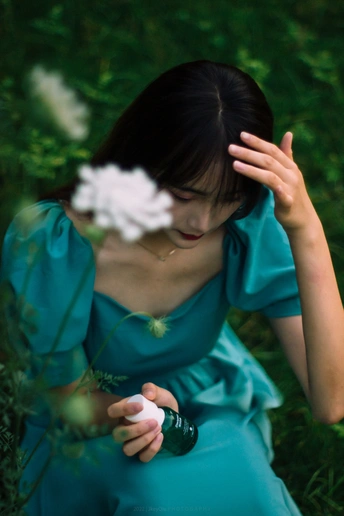 一位身穿蓝色连衣裙的年轻女子坐在绿草丛中 双手捂着脸