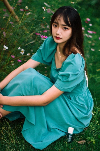 一个穿着蓝色连衣裙的年轻女子坐在绿草和鲜花的田野里