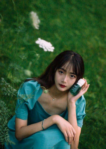 一位身穿蓝色连衣裙的年轻女子坐在绿草地里
