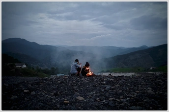 坐在篝火旁的夫妇 背景是山脉。
