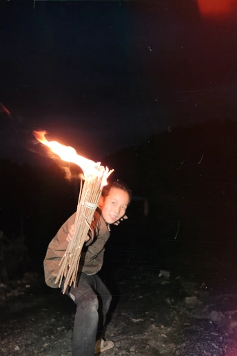 一个小女孩拿着一个火焰从其中发出的木棍 一个年轻男子在夜晚拿着火炬。