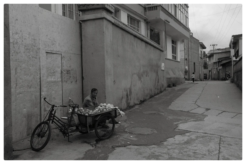 一个人在街头卖水果 旁边坐着一个男孩 一个黑白镜头