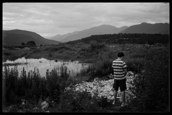 一个人站在一个田野里 注视着一个有山丘作为背景的湖泊。