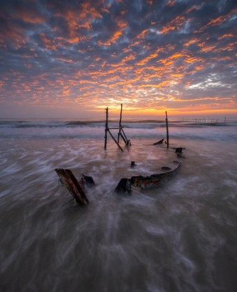 夕阳下海滩 一艘老船在水中 海洋上有波浪。