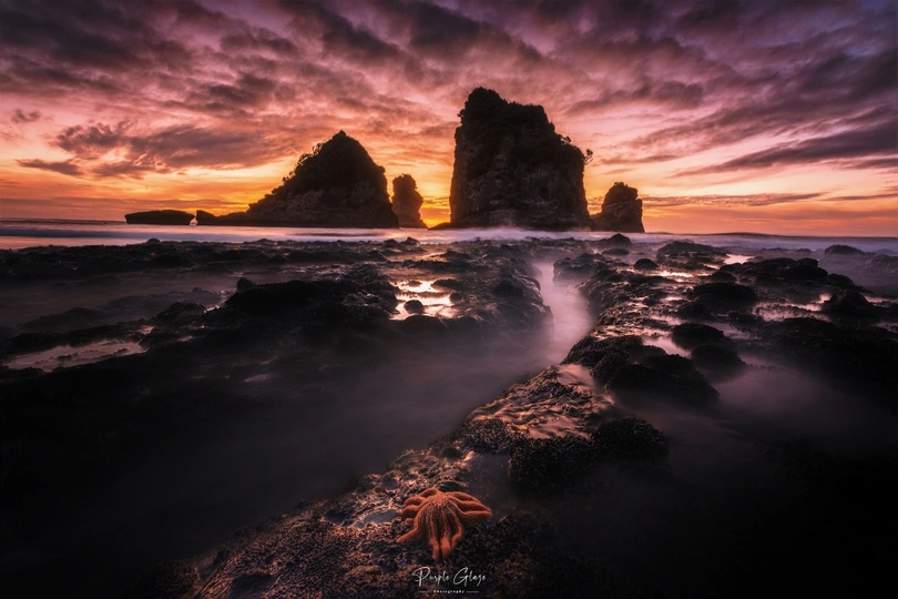 美丽的海滩日落 水中有岩石 前景中有海星。