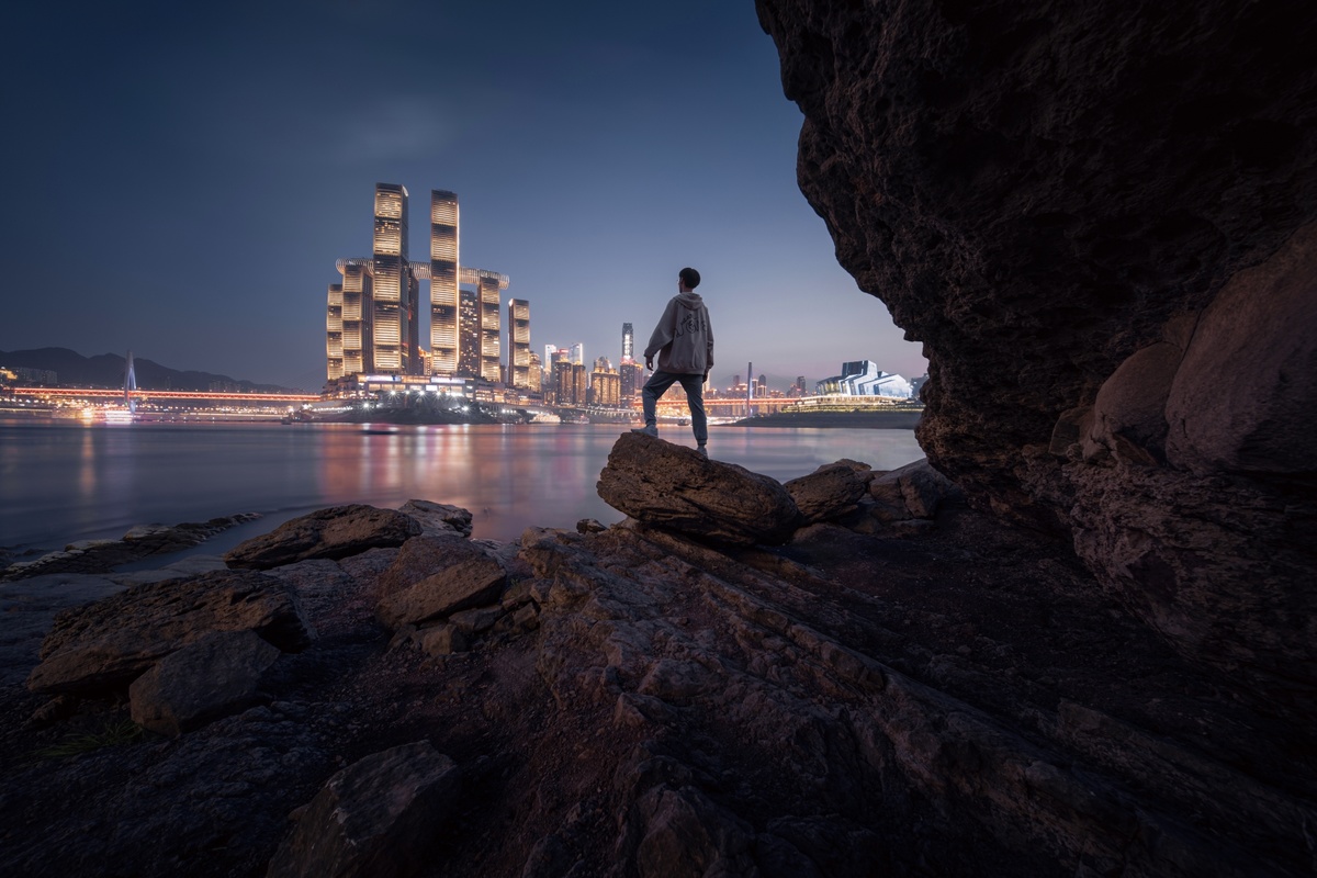站在海边的城市夜晚前的巨大岩石上的一个男人