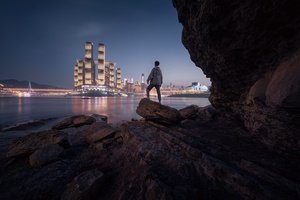 站在海边的城市夜晚前的巨大岩石上的一个男人