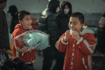 一个戴面具的年轻男孩拿着一个食物袋在街上 背景有其他人。