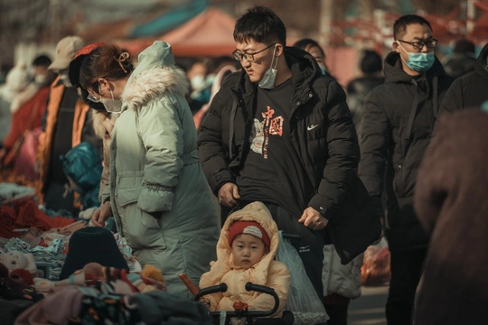 一位戴口罩的女人推着婴儿车穿过人群走在街上