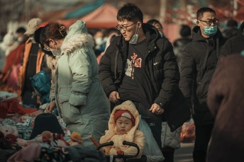 一位戴口罩的女人推着婴儿车穿过人群走在街上