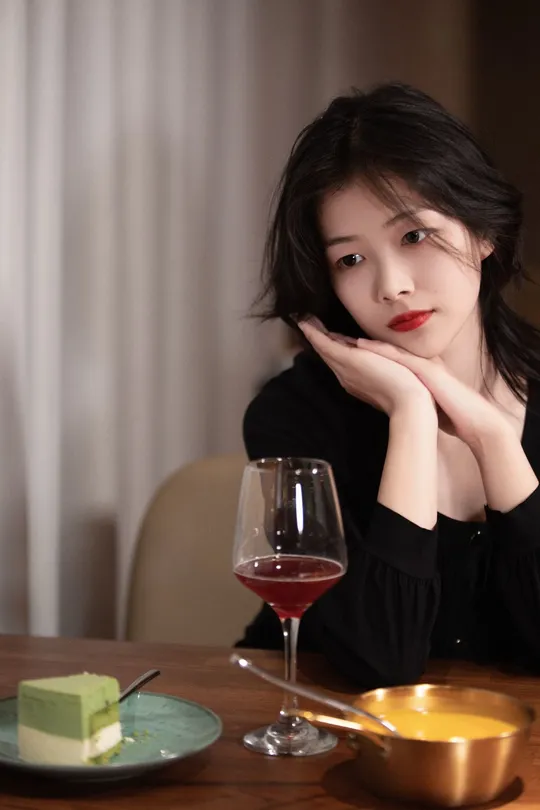 一个年轻女子手握红葡萄酒杯坐在桌子旁