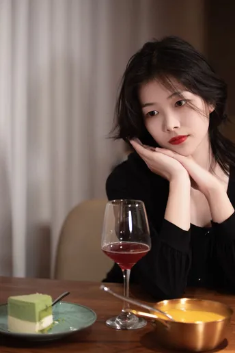 一个年轻女子手握红葡萄酒杯坐在桌子旁