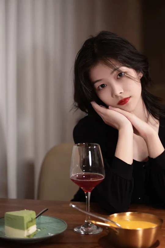 一位年轻女子端着一杯红葡萄酒坐在桌子旁