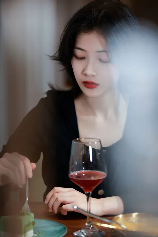 一个女性坐在桌子旁喝着一杯红葡萄酒