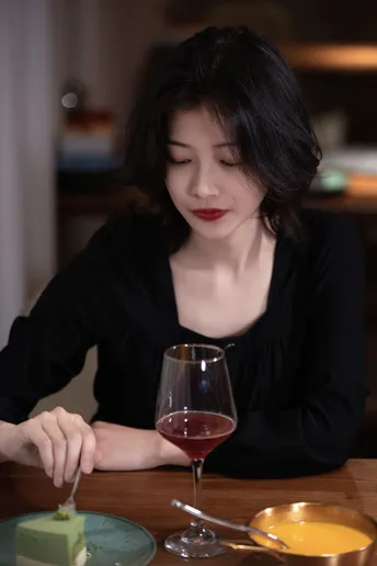 一个坐在桌子旁 盘子里有食物 杯子里有红酒的女士