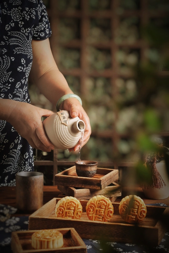 一位女性在木桌上倒入茶水到白色杯子中 旁边放着小盒饼干。