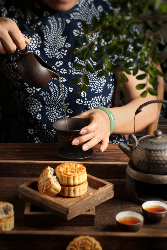 一位女士从茶壶中倒了一杯茶 放在木制桌子上的一小盘糕点上。