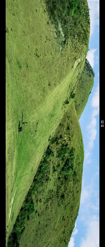 一架飞机飞越一座大山丘 山丘上长着绿色的草地 背景中有一座山。