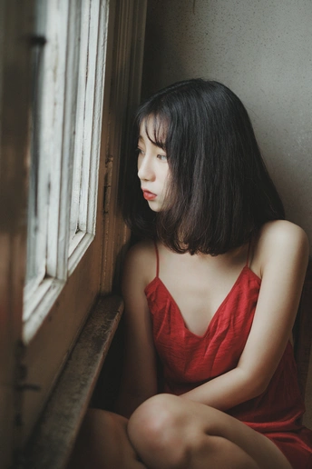 一个穿着红裙子的年轻女子坐在窗台上向外看