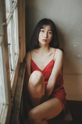 一位穿着红裙子的年轻女子坐在窗户旁边向外看