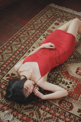 一个穿着红裙子的年轻女子躺在红色地毯上 旁边有一个红色枕头。