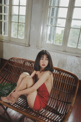 一位穿着红衣服的年轻女子坐在一个有很多窗户的房间里的一张木凳上