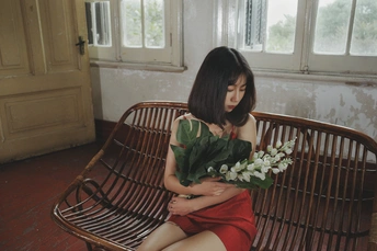 一位穿着红裙子的年轻女子抱着一束白花坐在木凳上