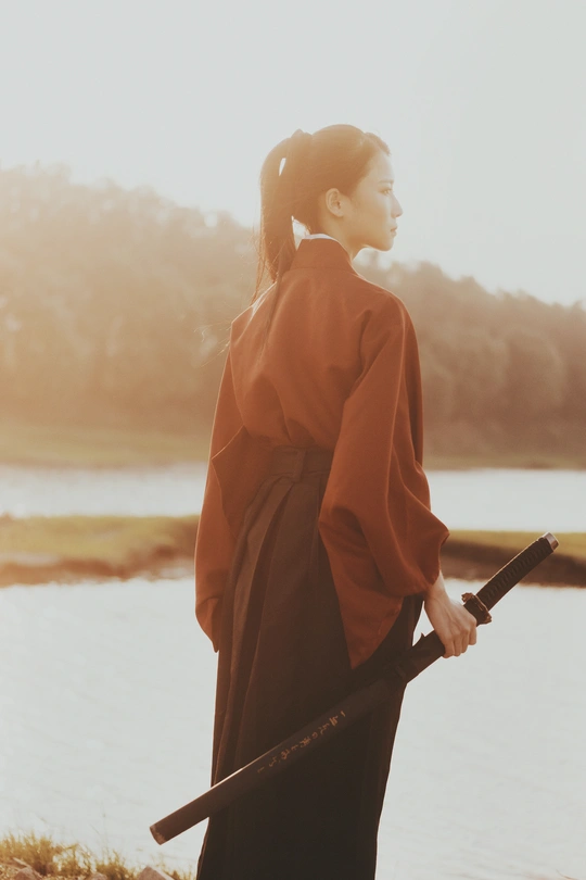 一位穿着红色和服的年轻女子打着雨伞在水边走。