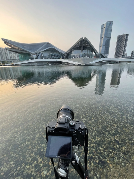 在一座水域前方 有一架三脚架上的相机 背景中有建筑物和城市。