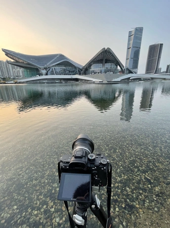 在一座水域前方 有一架三脚架上的相机 背景中有建筑物和城市。