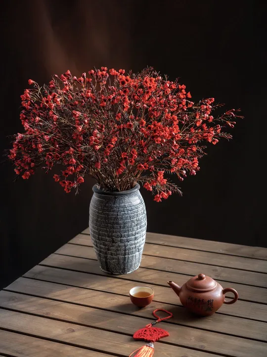 一个木制桌子 上面放着一个装满红花的花瓶和一个小杯子。