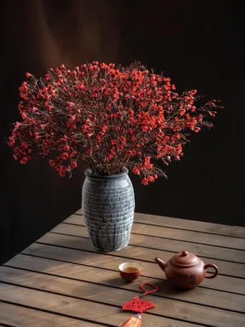 一个木制桌子 上面放着一个装满红花的花瓶和一个小杯子。