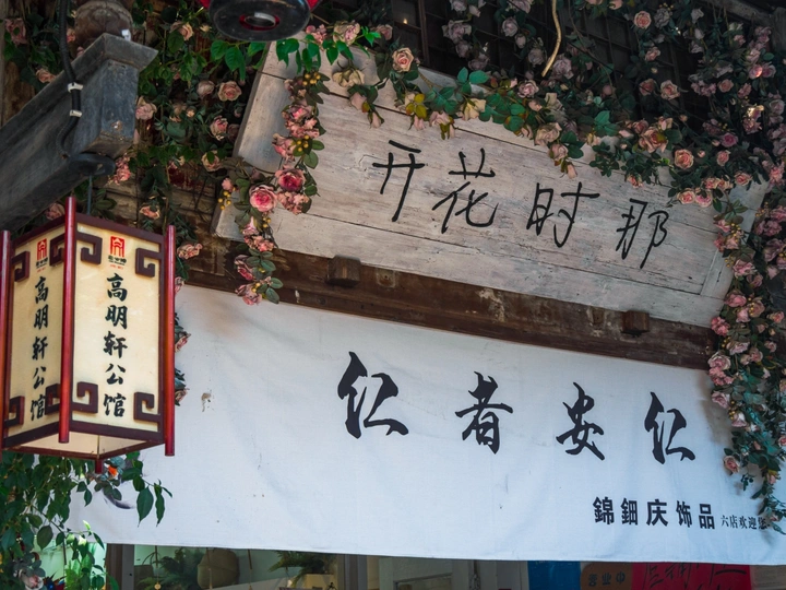 一家餐厅外挂着一块有中文书写的木制招牌 墙上开着花。