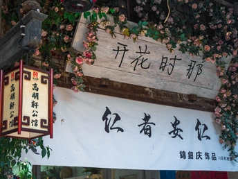 一家餐厅外挂着一块有中文书写的木制招牌 墙上开着花。