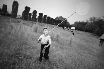 一个小男孩在草地上拿着风筝 背景有人在玩耍。