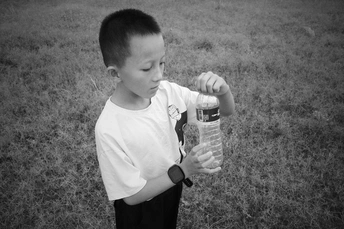 一张黑白照片 一个年轻男孩站在草地上 手里拿着一个塑料水瓶。