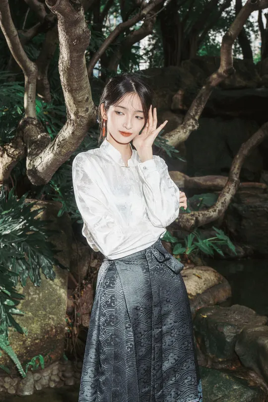 一位穿着白色衬衫和裙子的女孩站在一棵树下