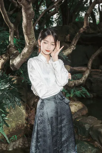 一位穿着白色衬衫和裙子的女孩站在一棵树下