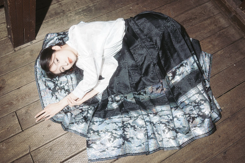 一个穿着黑色连衣裙的年轻女子躺在蓝色的毛毯上 躺在木地板上