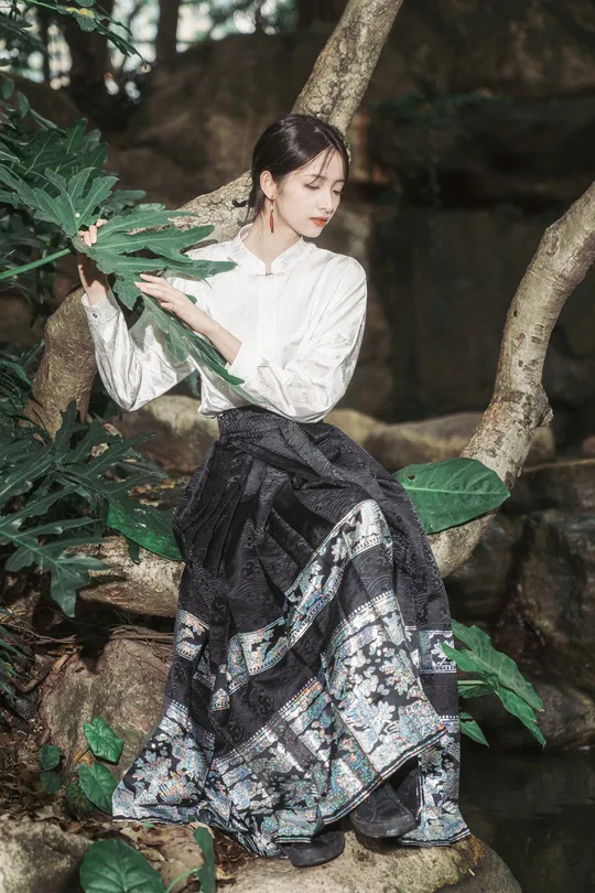 美丽的女孩穿着传统服装坐在岩石上 森林中 并拿着一片叶子。